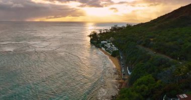 Dalgalar yeşil dağın altındaki kumlu sahile doğru akar. Hawaii, ABD 'nin günbatımı manzarası.