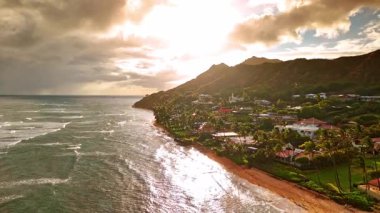 Dağlarla çevrili ikonik yeşil rıhtım bölgesi. Rüzgarlı bir günde dalgalar kıyıya vurur ve palmiye ağaçları bükülür. Honolulu, Hawaii, ABD 'nin günbatımı manzarası. Hava perspektifi.
