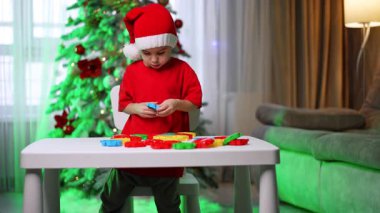 Masada oynayan dört yaşında, Noel Baba şapkalı bir çocuk. Küçük çocuk evde bulmacalarla oynuyor..