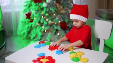Noel Baba şapkalı şirin çocuk masada oyuncaklarla oynuyor. Odaklanmış erkek bebek renkli yapboz parçalarıyla inşa eder.