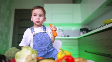 Dört yaşında sevimli bir çocuk büyük bir havuç yiyor. Yeni yürümeye başlayan çocuk çok çeşitli sebzelerle masada oturuyor. Düşük açı görünümü.