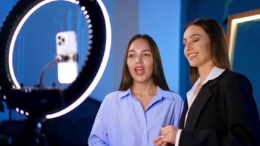 Yüzük lambasının yanında sohbet eden kadınlar. İki kadın bir stüdyo ortamında güçlendirilmiş ışıklandırma için halka ışığını kullanırken sohbet ediyorlar..