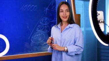 Dinamik sınıf sunumu. Genç bir kadın, elinde kalemle eğitim malzemelerini sunuyor ve öğretme becerilerini gösteriyor..