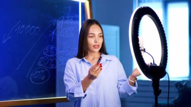 İnteraktif dijital ders. Genç bir kadın, istatistikleri gösteren bir karatahta ve halka ışığıyla çevrimiçi bir ders veriyor..