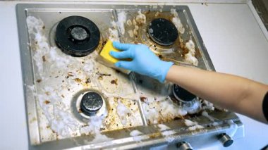 Etkili bir şekilde sobayı temizliyorum. Elinde süngerle yağlı bir mutfak sobasını ovalayarak pislik ve tortuyla kaplayarak temizleme çabalarını gösteriyor..