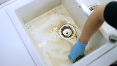 Kirli bir mutfak lavabosunu özenle temizlemek. Kirli bir mutfak lavabosunu süngerle temizleyip parlamasını sağlamak isteyen bir insan..