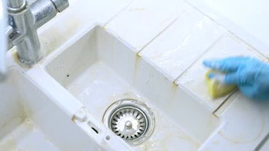 Mutfak lavabosunu sabunlu suyla temizlemek. Mavi eldivenli biri kirli bir mutfak lavabosunu süngerle temizler, yağ ve kiri etkili bir şekilde temizler..