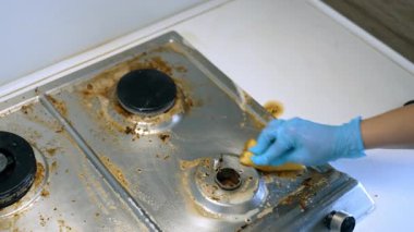 Yağlı bir mutfak ocağını temizliyorum. Eldiven giyen biri kirli bir sobayı temizler, mutfak temizliği sırasında yemek lekelerini ve yağları temizler..