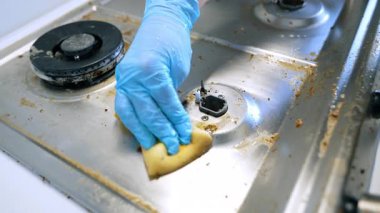 Sünger ve eldivenli temiz ocak. Mavi eldivenli bir insan, yağlı bir sobanın üstünü süngerle ovalayarak mutfak ortamındaki yemek artıklarını temizler..