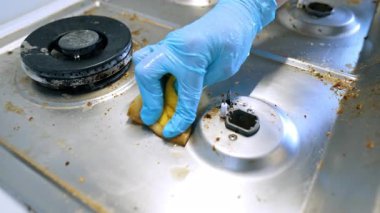 Mutfak sobasını özenle temizliyorum. Mavi eldiven giyen biri kirli bir fırın yüzeyini ovalayarak besin kalıntılarını ve lekeleri etkili bir şekilde temizler..