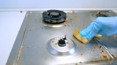 Mutfakta sobanın üstünü temizliyorum. Mavi eldivenli bir insan mutfakta kirli bir sobayı temizler. Yağ ve yemek artıklarını etkili bir şekilde temizler..