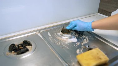 Mutfak alanında bir sobayı temizliyorum. Birisi yağlı bir sobayı süngerle ovalayarak lekeleri ve kiri temizliyor ve temiz bir yemek yüzeyi sağlıyor..