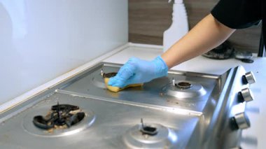 Mutfak sobası yüzeyi temizliyorum. Mavi eldiven giyen biri paslanmaz çelik ocağı süngerle temizler. Mutfağı temiz ve hijyenik yapar..