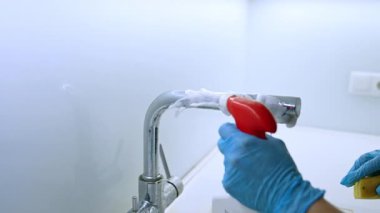 Musluk temizliği için köpük spreyi. Eldiven takan biri mutfak musluğunu köpük spreyiyle temizler. Parlak ve hijyenik bir son sağlar..