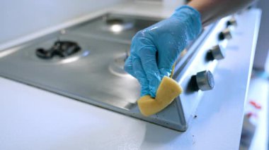 Mutfak sobasını özenle temizliyorum. Eldiven giyen bir insan paslanmaz çelik bir ocağı süngerle temizler ve mutfak yüzeyinin düzenli olmasını sağlar..