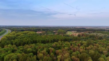 Geniş yeşil orman manzarası. Açık mavi gökyüzünün altında yemyeşil orman ufuk boyunca uzanır. Yuvarlanan tepeler ve bir otoyol yakınlarda görünüyor..