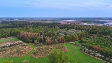 Yeşil tarlalar ve ağaçlar. Çeşitli ağaçlar, tarlalar ve uzak sanayi yapıları olan yeşil bir arazinin havadan görünüşü.