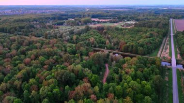 Gün batımında orman. Uçsuz bucaksız bir orman rengarenk bir günbatımının altında yayılmış ağaçlar, yollar ve açık arazilerle uzanır..