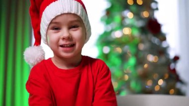 Bayram kıyafetli bir çocuk. Kırmızı gömlekli ve beyaz şapkalı bir çocuk bayram süslemeleri ve ışıklarıyla çevrili iken hediyeleri sevinçle açıyor..