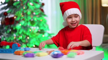 Evde çocukların tatil eğlencesi. Neşeli bir çocuk süslü bir Noel ağacının yanında renkli mankenlerle oynarken neşeli bir şapka takar..