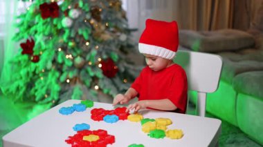 Çocuk renkli bloklarla oynuyor. Kırmızı elbiseli küçük bir çocuk, beyaz bir masada renkli bloklarla oynuyor. Etraflarında şenlik süsleri var..
