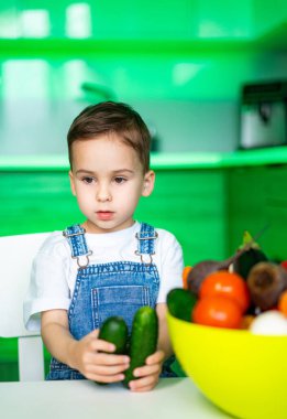 Küçük çocuk mutfakta salatalık tutuyor. Küçük bir çocuk mutfakta oturmuş, elinde meyve dolu iki salatalıkla sağlıklı beslenme alışkanlıkları sergiliyor..