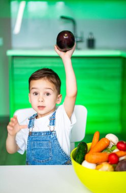 Çocuk canlı bir mutfakta sebze tutuyor. Genç bir çocuk rengarenk bir mutfak ortamında taze sebzelerle çevriliyken patlıcan yetiştirir..