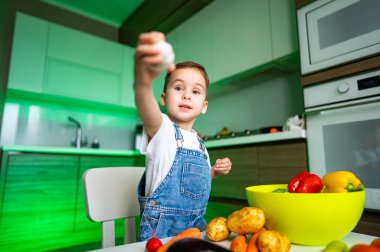 Çocuk mutfakta yemek yapmayı seviyor. Tulumlu çocuk sebzelerle oynuyor. Parlak ve canlı bir mutfak ortamında aşçılık yaratıcılığını keşfediyor..