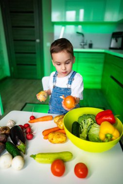 Çocuk mutfakta sebze keşfediyor. Genç bir çocuk modern bir mutfakta renkli sebzeleri inceler, merakını ve sağlıklı yiyeceklerle olan bağlılığını gösterir..