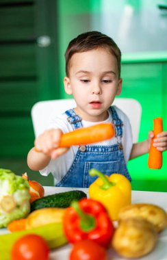Çocuk sebzeleri mutfakta keşfediyor. Genç bir çocuk, taze ürünlerle çevrili modern bir mutfak ortamında renkli sebzeleri merakla inceliyor..