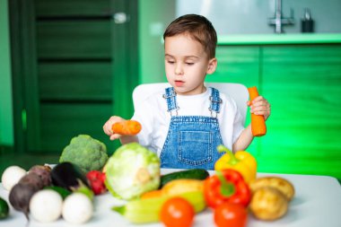Çocuk sebzeleri mutfakta öğreniyor. Genç bir çocuk modern bir mutfakta taze sebzeleri, renkli ürünler arasında bir havuca odaklanarak inceliyor..