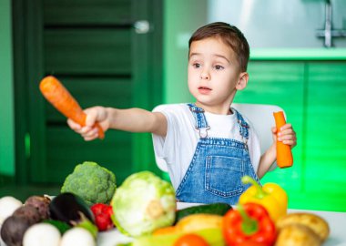 Çocuk sebzelerle yemek yapmayı seviyor. Genç bir çocuk parlak bir mutfakta mutfak becerilerini keşfederken renkli sebzelerle oynuyor..