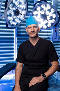 Yetenekli cerrah ameliyata hazırlanıyor. Siyah önlüklü ve mavi şapkalı bir cerrah ameliyata hazır bir şekilde bir ameliyathanede güven içinde oturur..