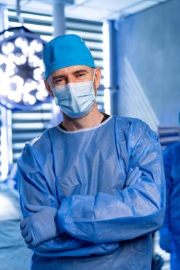 Mavi önlüklü cerrah hazır. Mavi önlüklü, maskeli ve eldivenli bir sağlık uzmanı cerrahi bir ortamda güvenle ayakta duruyor..