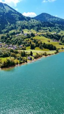 Dağlarda yeşil ormanlarla kaplı bir göl. Köy, pitoresk su manzarasının kıyılarına saçılmıştır. Üst Manzara. Dikey video.