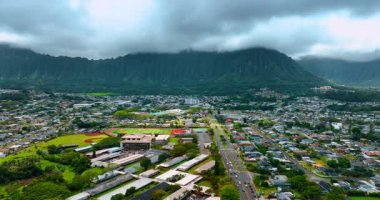 Honolulu 'nun yeşil şehir manzarası, Hawaii, ABD. Hawaii Üniversitesi 'nin stadyumuna yaklaşan insansız hava aracı görüntüleri. Yeşil engebeli dağlar manzaranın etrafını sardı. Şiddetli bulutlu gökyüzünü kaplıyor.