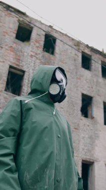 Koruyucu kıyafetli ve gaz maskeli bir çevreci. Gaz maskeli adam neredeyse yıkılmış bir bina.