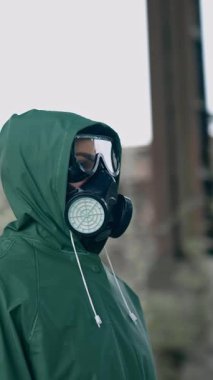 Gaz maskeli ve koruyucu giysili bir adam. Gaz maskeli ve pelerinli bir adam terk edilmiş fabrikada kimyasal koruma için.