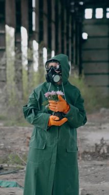 Koruyucu üniformalı ve gaz maskeli bir adam. Terk edilmiş hangarda duran silahlı vahiysel karakter.