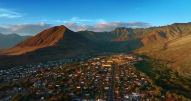 Dağlardaki Honolulu 'nun alçak katlı panoramasının üzerinde uçuyorlar. Çıplak kayalarla çevrili yerleşim alanının gün batımı görüntüsü.