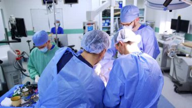 Bir hastayı ameliyat eden mavi cüppeli iki erkek doktorun dikiz görüntüsü. Cerrahide ekipmanlara yardım etmek.