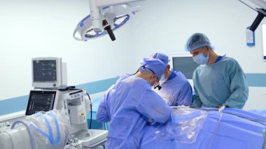 Modern cerrahi odasında üç erkek doktor ameliyat yapıyor. Doktor enstrüman tüpü ile hareket eden bir alet ve kan kullanır..