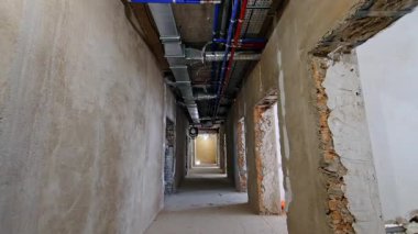 Uzun koridordaki hareketlilik yeniden yapılandırılıyor. Koridorun tavanında bitmemiş duvarlar ve borular var..