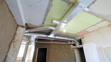 Yenilenmiş odanın tavanında farklı renkte paneller var. Düşük açı. İnşaattaki metal ve plastik borular..
