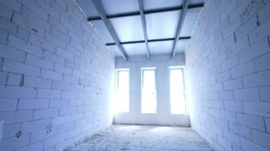 Parlak gün ışığı üç dar pencereden odaya girer. Odada beyaz tuğla duvarlar var. İnşaat konsepti.