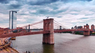 Birden fazla araba ve insanlar güzel Brooklyn Köprüsü 'nün yanından geçiyor. Manhattan Köprüsü 'nden görüntü geliyor. Gökyüzünü kaplayan dramatik bulutlar.