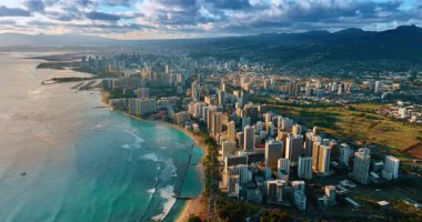 Dalgalar yavaşça Waikiki, Honolulu, Oahu, Hawaii, ABD 'nin kumlu sahillerine doğru ilerliyor. Şehrin engin manzarası dramatik bulutlar altında..