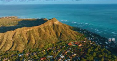 Batan güneşin ışığında Diamond Head Krateri. Yerleşim yerleri, volkanik kayaların dibindeki yeşillikte. Pasifik Okyanusu arka planda. Hava görünümü.