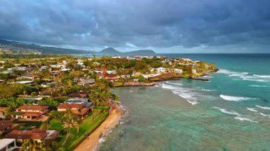 Hawaii, ABD 'nin pitoresk sahillerindeki büyüleyici yemyeşil villalar. Dalgalar kumlu plaja doğru akar. Panoramanın üstündeki gökyüzünü kaplayan ağır bulutlu bir manzara. Hava perspektifi.