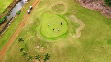 Açık yeşil alanda dört adam duruyor. Sporcular derenin yanında golf oynarlar. Hawaii, ABD. Üst görünüm.